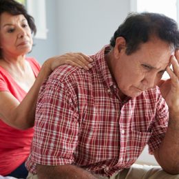Man holding head while wife stands behind comforting him