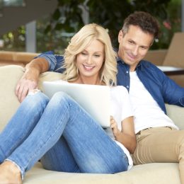 happy smiling couple with woman looking at computer while cuddling with man on couch