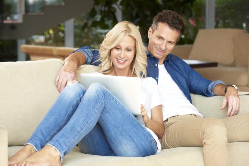 happy smiling couple with woman looking at computer while cuddling with man on couch