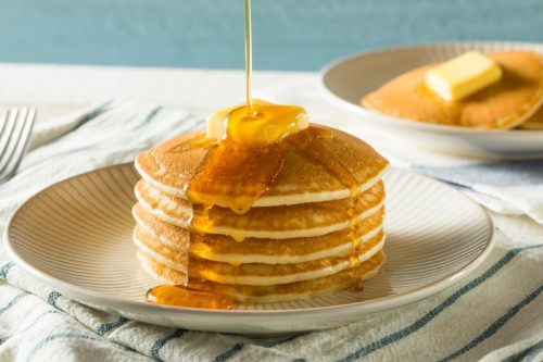 stack of pancakes on a plate with butter and maple syrup being drizzled on top