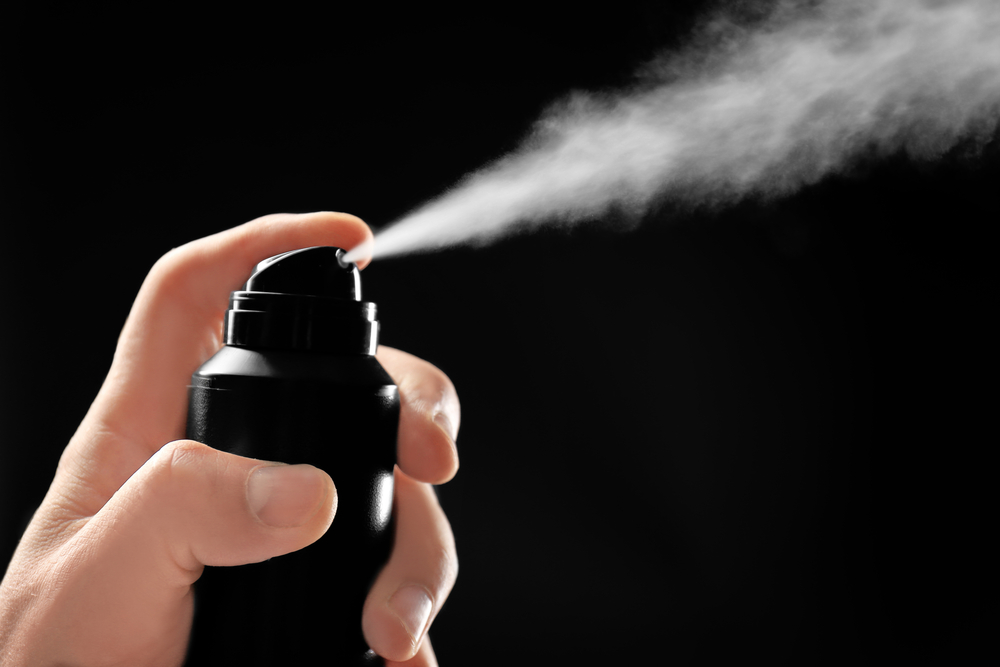 A can of deodorant or antiperspirant being sprayed over a black background