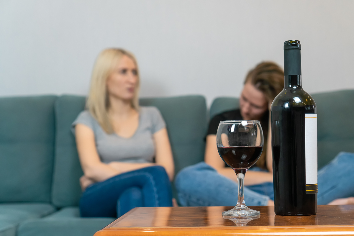 две млади жени, седнали на дивана и разговарящи сериозно с бутилка вино на преден план
