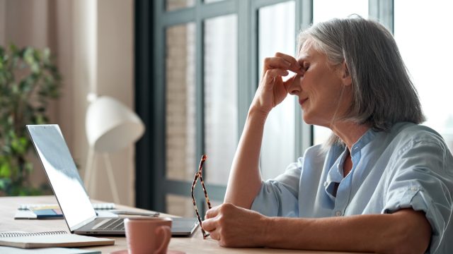 older white woman looking worn out sitting in front of her computer rubbing her eyes