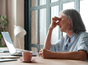 older white woman looking worn out sitting in front of her computer rubbing her eyes