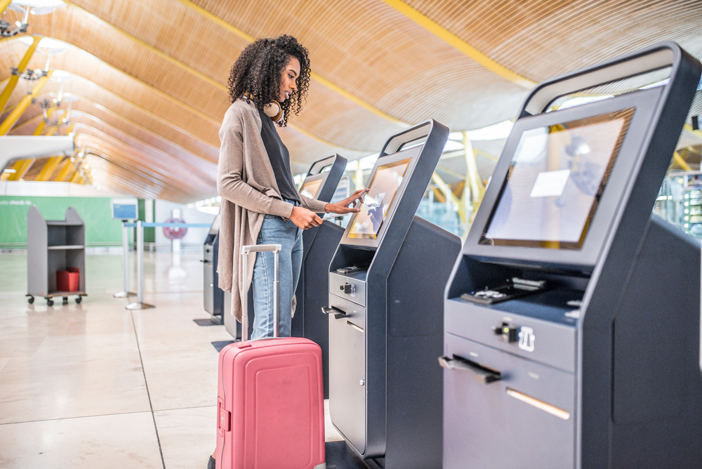 A young woman with a suitcase printing her boarding pass for a flight at a kiosk in the airport