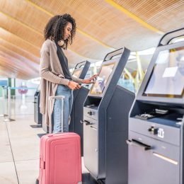 A young woman with a suitcase printing her boarding pass for a flight at a kiosk in the airport