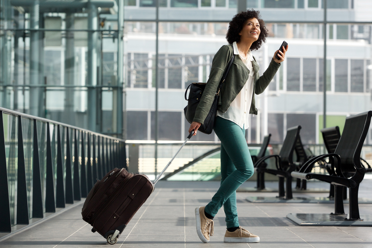 Một phụ nữ trẻ vừa kéo vali qua sân bay vừa dùng điện thoại