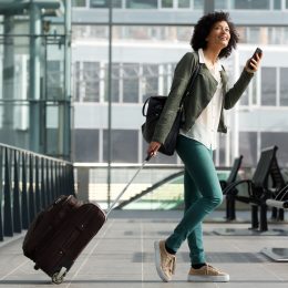 A young woman pulling her suitcase through the airport while using her phone