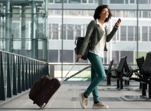 A young woman pulling her suitcase through the airport while using her phone