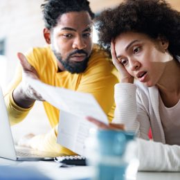 couple feeling frustrated while paying their bills over laptop at home