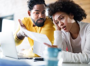 couple feeling frustrated while paying their bills over laptop at home