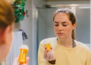 Woman in Bathroom Looking at Pill Bottle