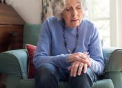 A senior woman sitting in a chair holding her hand, noticing symptoms of Parkinson's disease