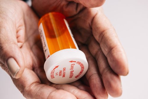 lady hands holding a bright red orange prescription medication pill bottle.