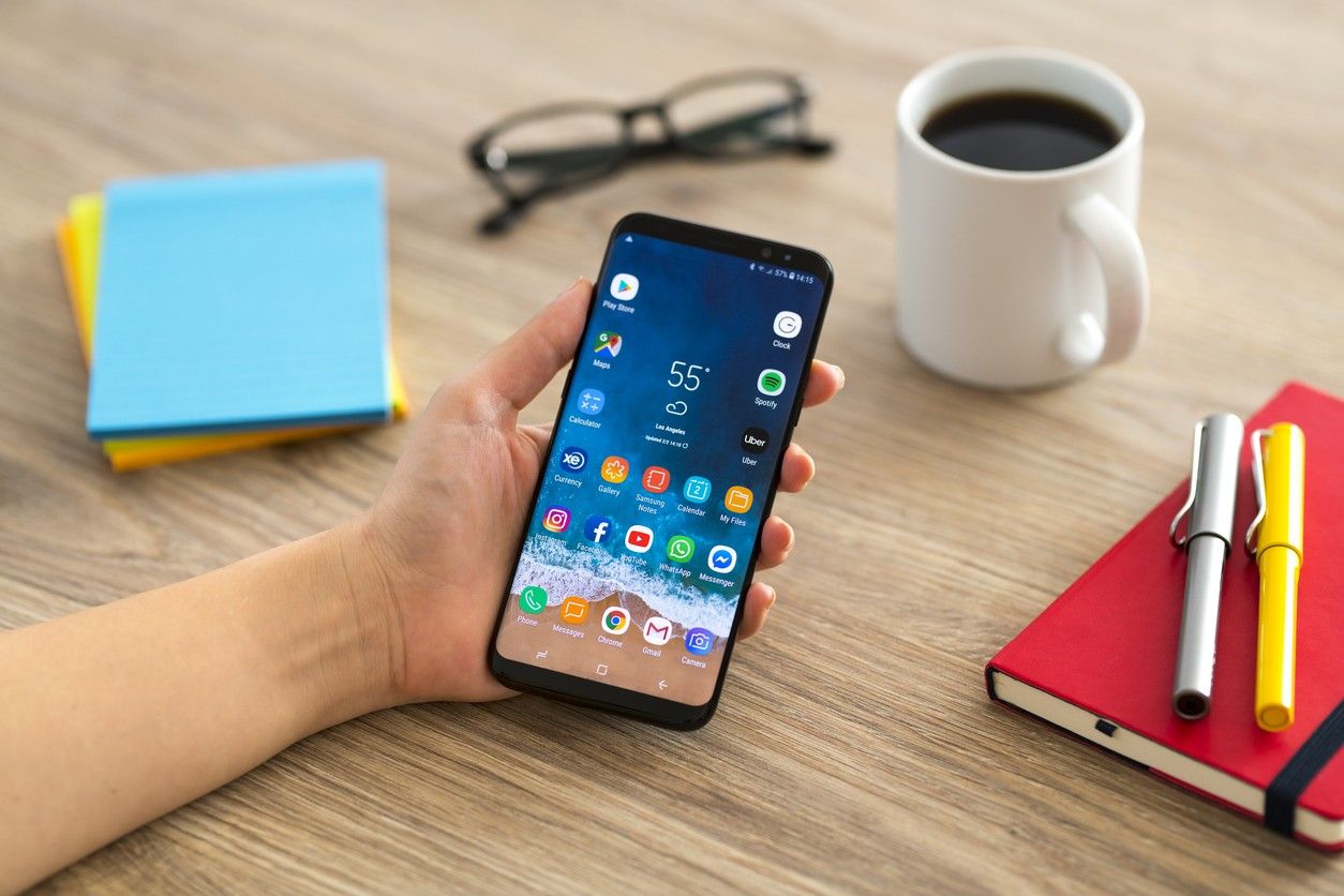 A close-up of a hand holding an Android phone on a desk