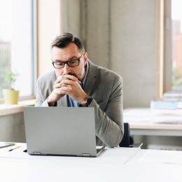 Thoughtful middle aged handsome businessman in shirt working on laptop computer in office. Man working in office