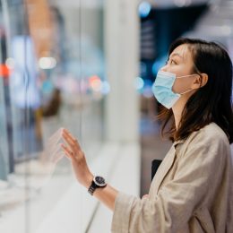 woman with face mask looking at shop window while walking in the city at night