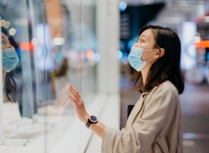 woman with face mask looking at shop window while walking in the city at night