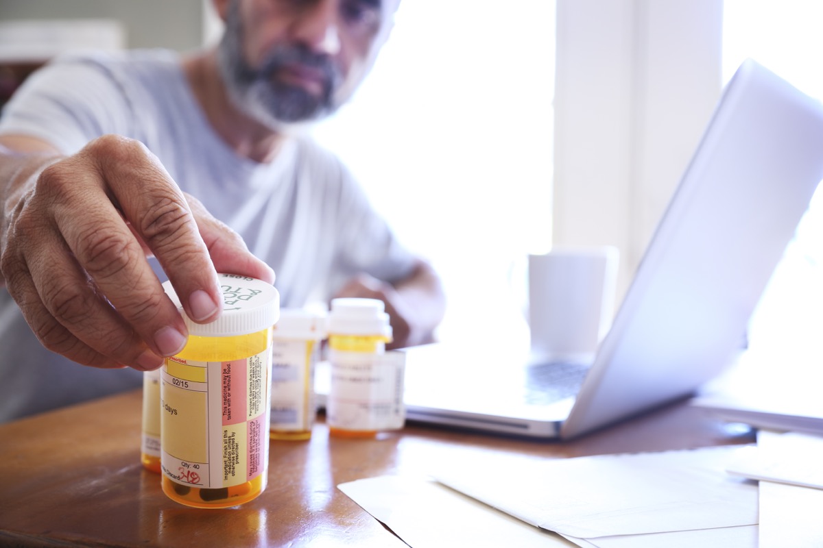 a man in his late 50s grabs one of his prescription medicine bottles as he sits at his dining room table
