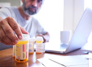 man in his late fifties reaches for one of his prescription medication bottles as he sits at his dining room table