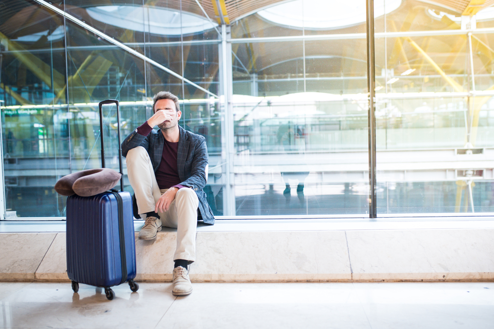 Un bărbat care stă la aeroport cu o privire tristă pe față din cauza întârzierii sau anulării unui zbor