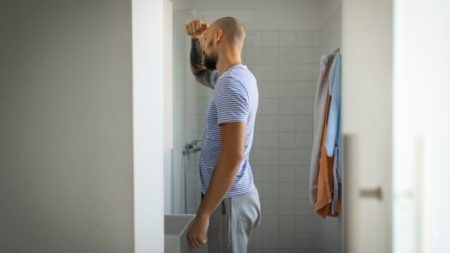 man standing in the bathroom, looking in the mirror, getting ready for work.