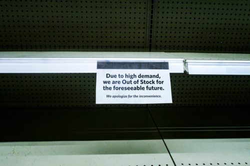 COVID-19 Coronavirus "OUT OF STOCK" sign on completely empty retail supermarket shopping food and groceries merchandise products display shelves.