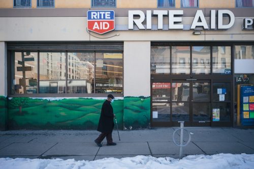 A man wearing a mask walks in front of a Rite Aid Pharmacy in East Harlem.