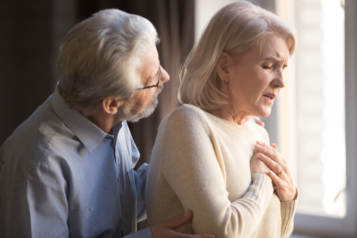 older white woman clutching her chest as her husband looks worried behind her