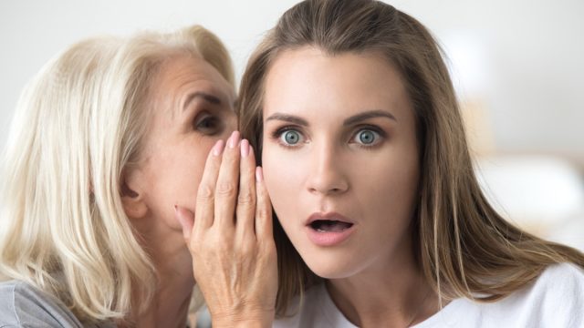 older woman telling secret to younger woman