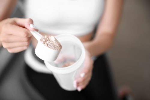 Frau schöpft Proteinpulver in einen Shaker