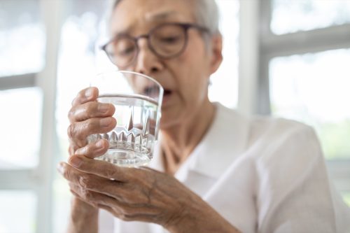 Ältere Frau, die ein Glas Wasser hält und aus Angst vor der Parkinson-Krankheit zittert