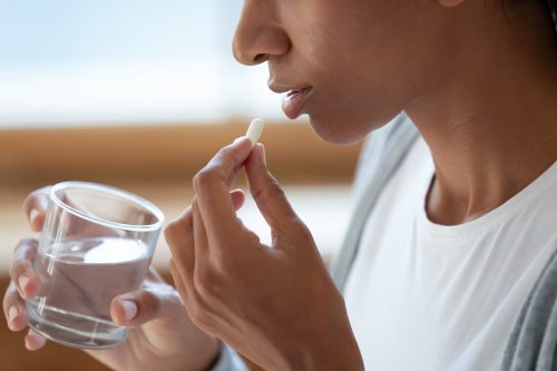 Close-up of a girl holds a glass of water and white pills in her mouth.