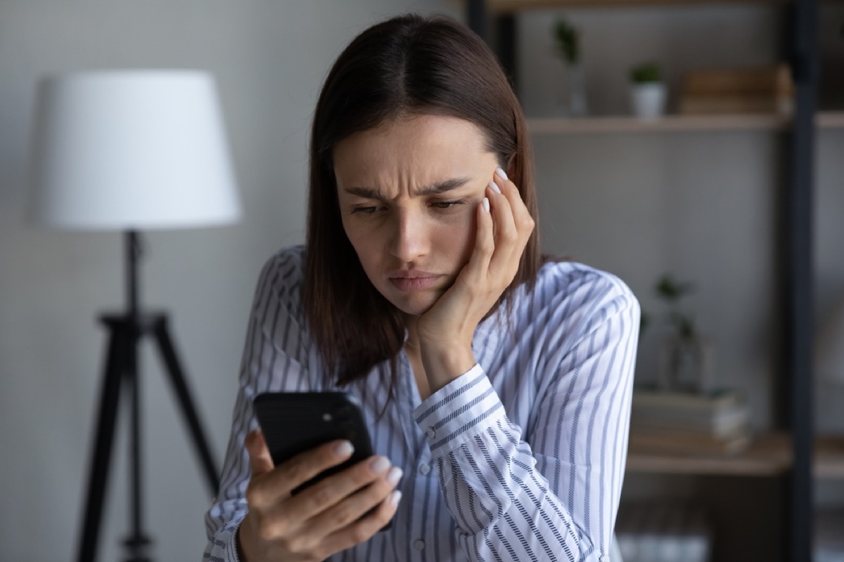 A woman looking upset and upset with her hand on her face and her phone in her hand