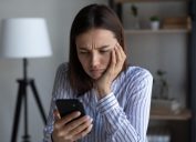 woman looking annoyed and upset with her hand on her face and her phone in her hand