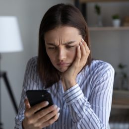 woman looking annoyed and upset with her hand on her face and her phone in her hand