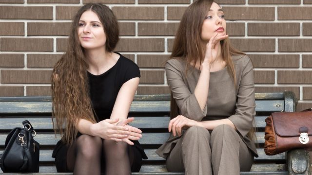 two women sitting on a bench and one is ignoring the other