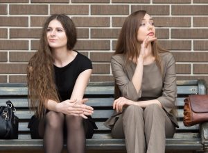 two women sitting on a bench and one is ignoring the other
