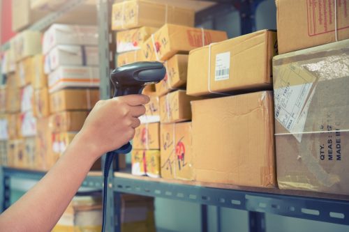 Postman worker scanning package with barcode scanner in warehouse for delivery.