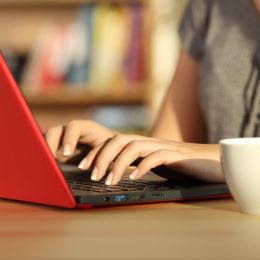 Close up of girl hands writing in a red laptop on a table at home with a warm light and a colorful background