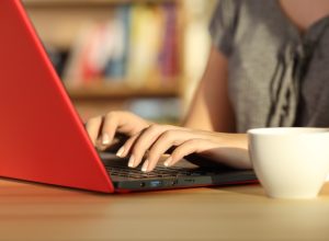 Close up of girl hands writing in a red laptop on a table at home with a warm light and a colorful background