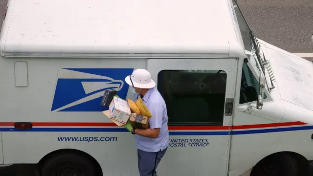 United States Postal Service USPS mailman wears a mask and gloves while carrying a load of parcels from a mail truck during the COVID-19 coronavirus pandemic.
