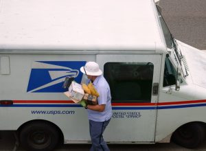 United States Postal Service USPS mailman wears a mask and gloves while carrying a load of parcels from a mail truck during the COVID-19 coronavirus pandemic.