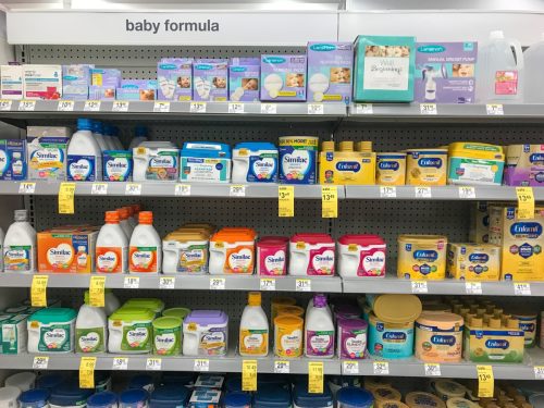 Various baby formula packages on the shelves of a Walgreens drug store.