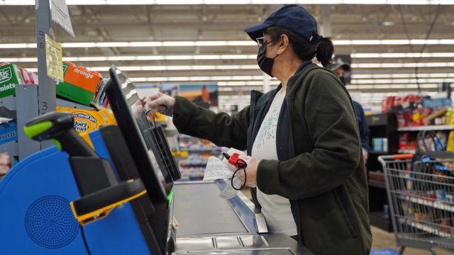 Masked and gloved woman uses the self checkout
