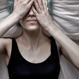 young woman lying down with her hands covering her face feeling unwell