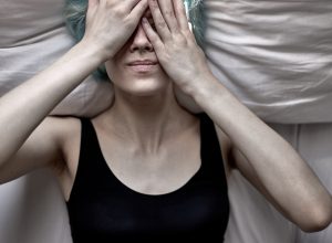 young woman lying down with her hands covering her face feeling unwell
