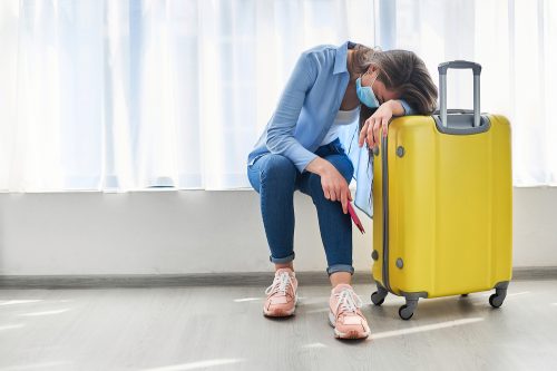 A young woman sitting next to her luggage in an airport looking sad after her flight was delayed or canceled