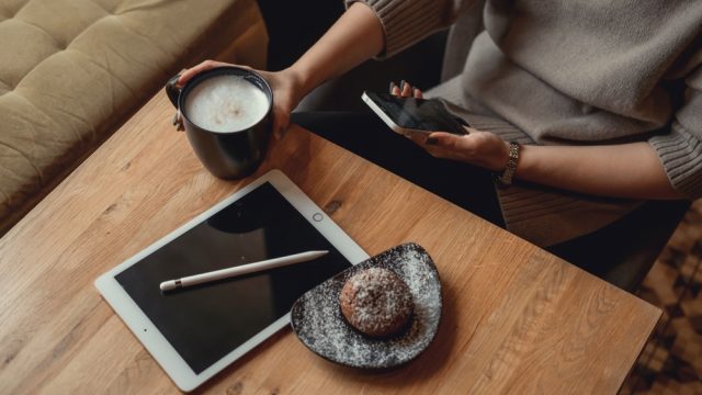 A woman sitting in a cafe using an iPhone and iPad while drinking coffee