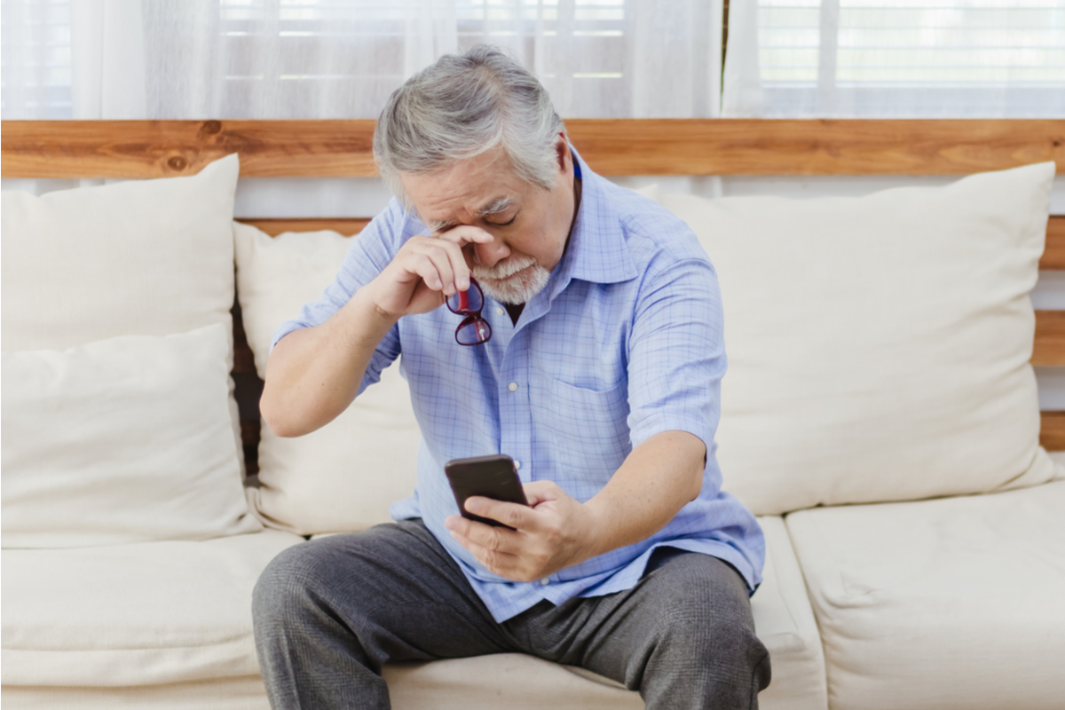 Un bărbat care stă pe canapea ținând telefonul și frecându-se la ochi